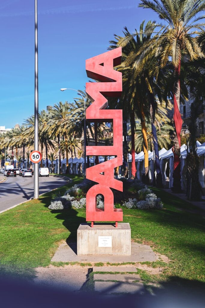PALMA sculpture on a sunny day in Palma de Mallorca, Spain with palm trees and a clear sky.